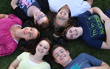 A few SUCCESS students in a circle laying on the grass with their heads together.