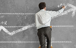 Man standing on a ladder in front of a chalkboard with an up arrow on the chalkboard